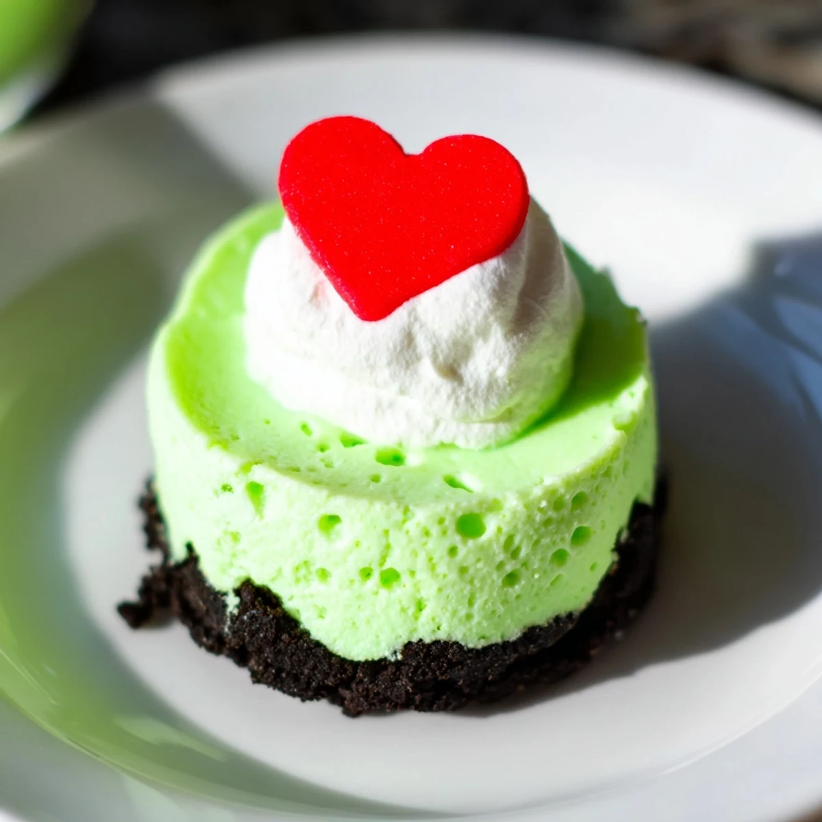Grinch Mini Cheesecakes, ready to eat, topped with whipped cream, sprinkles, and a red heart.