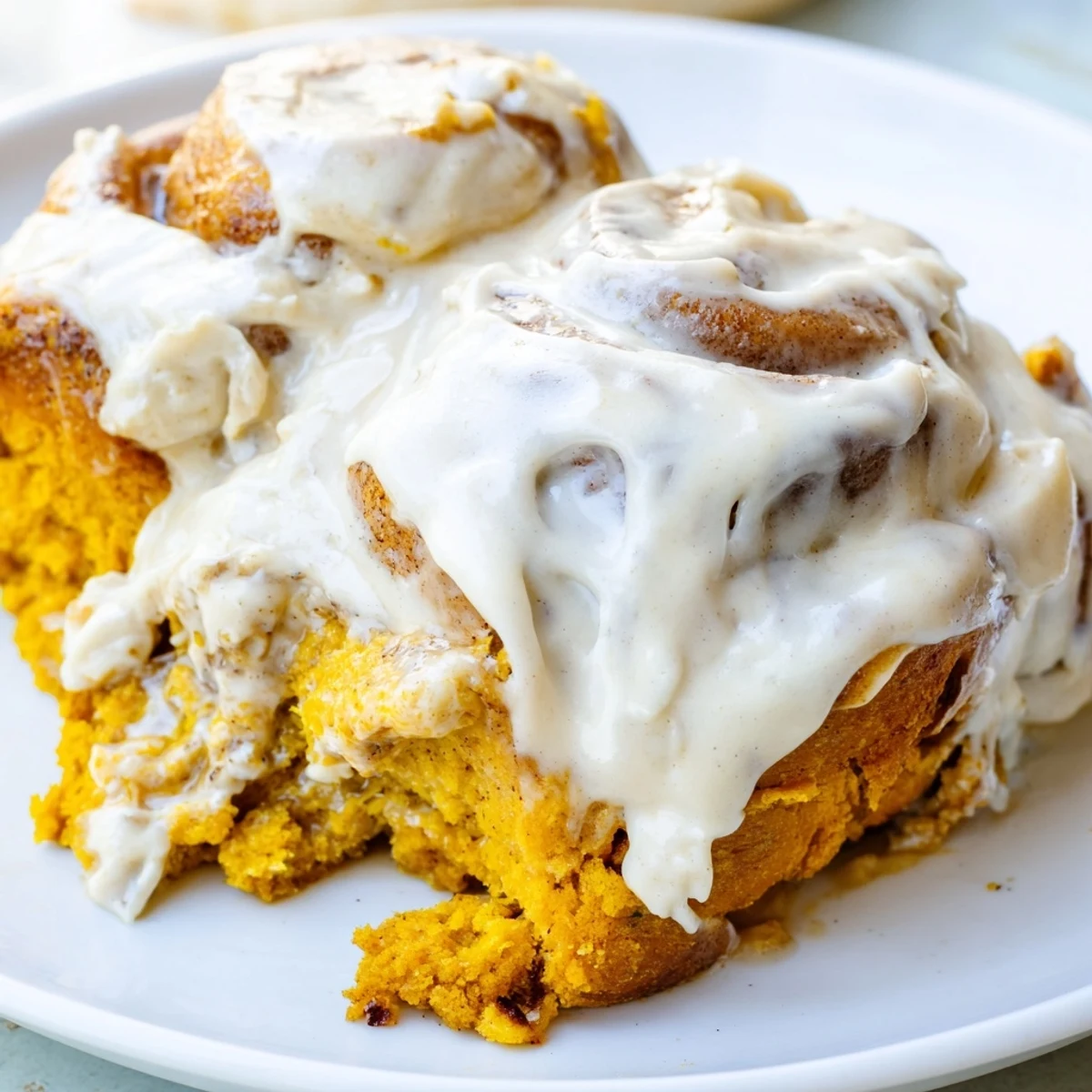 Warm, fluffy pumpkin cinnamon rolls glistening with cream cheese frosting, a fall breakfast delight.