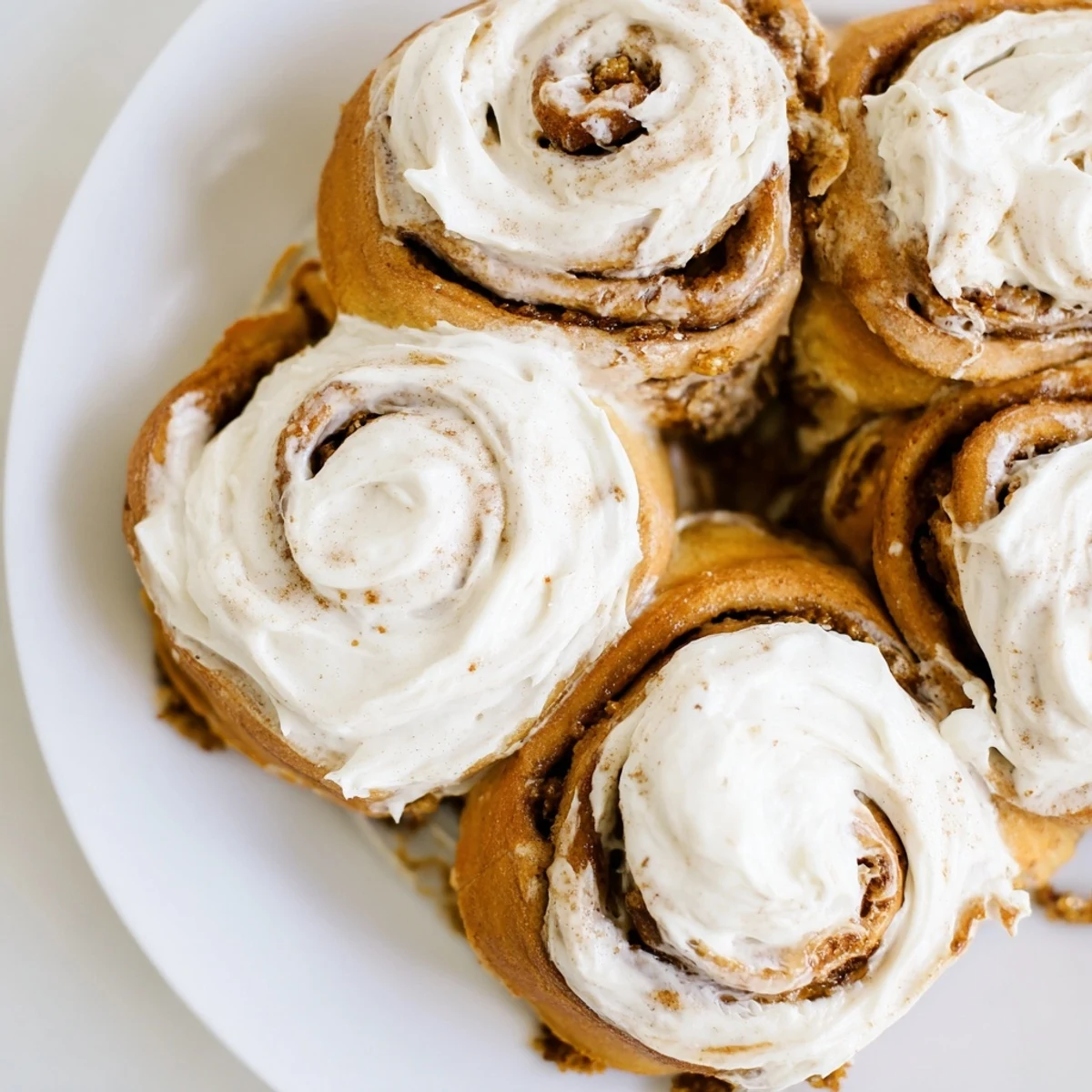Close-up of golden brown pumpkin cinnamon rolls, showing a soft, swirled interior and sweet glaze.