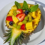A close-up of a refreshing Tropical Pineapple Fruit Boat overflowing with juicy fruit and mint garnish.