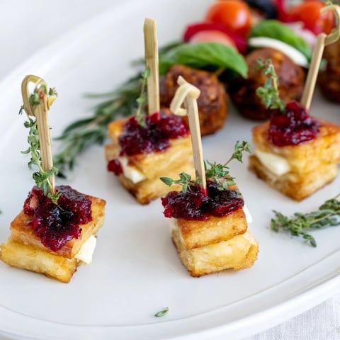 Festive Joy to the World Appetizer Trio: Golden cranberry brie bites, caprese skewers, and spiced meatballs arranged beautifully.