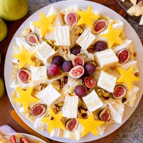 Festive Éclat dÉtoiles Planche de Noël showcasing cheeses, meats, fruit, and nuts, arranged beautifully in a starburst pattern.