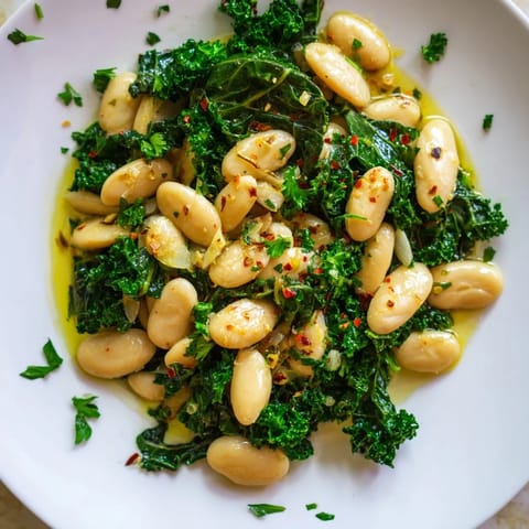 A close-up of Garlicky Beans with Winter Greens, glistening with olive oil and fresh parsley garnish.