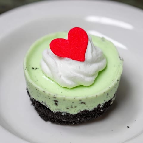 Vibrant green Grinch Mini Cheesecakes, beautifully frosted with whipped cream and sprinkles, ideal for Christmas.