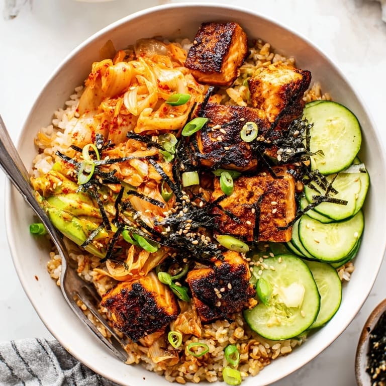Flavorful crispy salmon rice bowl garnished with fresh cucumber, creamy avocado, and nori.