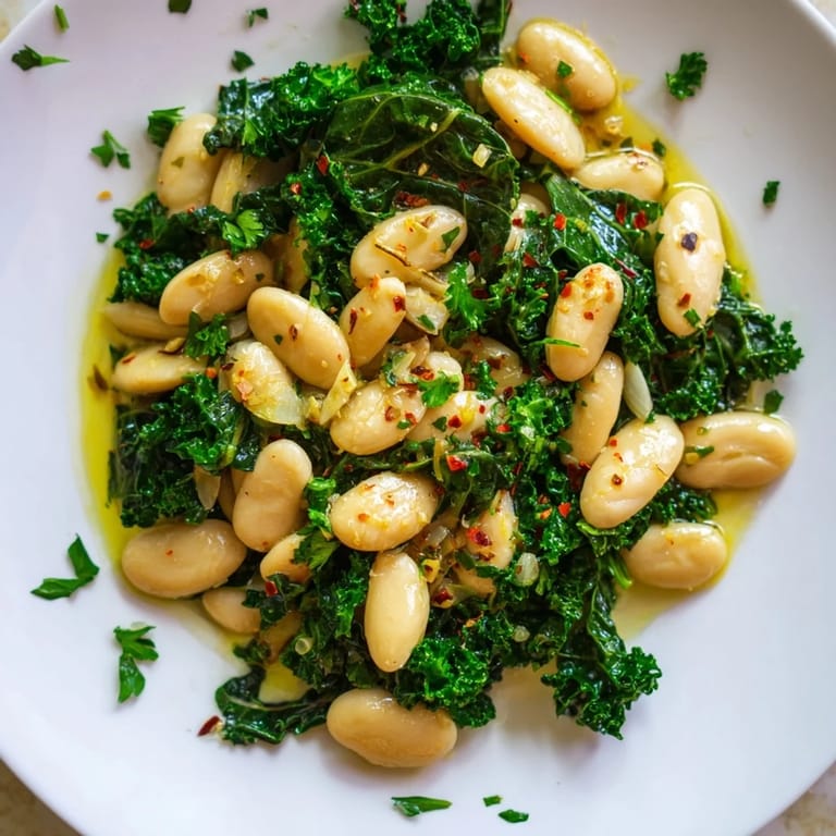 A close-up of Garlicky Beans with Winter Greens, glistening with olive oil and fresh parsley garnish.