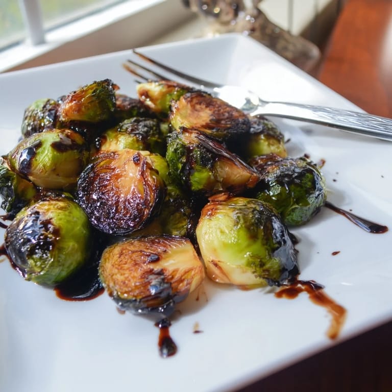 Freshly roasted Brussels sprouts with a caramelized exterior and tangy balsamic glaze on a white plate.